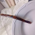 Elegant amber tortoise shell hair clip with gold metal spring on a white plate - Textured Brown