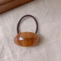 Amber acetate oval charm hair tie with dark brown elastic band on linen background - Caramel color