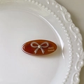 Detail of a brown amber oval hair clip with a rhinestone bow on a white ceramic plate - Caramel