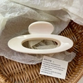 Macro shot of minimalist cream-colored oval hollow hair claw clip in a woven basket - Cream