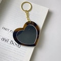 Makrodetail eines herzförmigen Schildpatt-Schlüsselanhängers auf einem Buch - Spiegel-Schlüsselanhänger (5.9cm*5.4cm 15g)