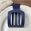 Close-up of matte dark blue hair claw with hollow square design on a white ceramic tray - Blue