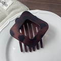 Dettaglio macro della molletta in resina tartarugata con design geometrico e forato - Marrone Rosso