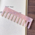 Close-up of marble pink cellulose acetate wide-tooth comb on an aesthetic book background - Pink