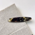 Dettaglio del fermaglio in acetato tartarugato con scritta dorata su lino - Ambra
