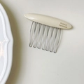 Dettaglio macro del pettine in acetato crema con logo dorato e denti in metallo argento - Bianco Latte