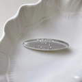 Macro shot of oval seashell texture hair clip with silver flakes on a white ceramic dish - Silver