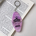 Porte-clés losange en acrylique marbre violet avec motif montagne sur fond de livre ouvert - Boucle Dorée / Violet