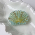 Macro di una molletta per capelli a conchiglia con linee dorate e strass su piatto - Verde