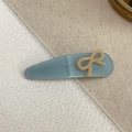 Detail of blue acetate hair clip with cream bow and handmade text on linen fabric - Lake Blue