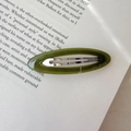 Close-up of olive green acetate oval hair clip with silver metal clip on a book page - Green