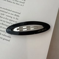 Minimalist black oval acetate hair clip with AMY BEAR logo on an open book - Black