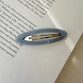 Light blue acetate oval BB hair clip with gold logo on an open book background - Blue