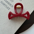 Detail view of a dark red bow hair claw clip with golden spring on a book surface - Red (78661)