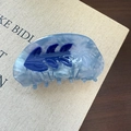 Macro detail of a light blue acetate hair claw clip with marble texture and floral pattern - Sunflower