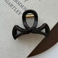 Détail d'une pince à cheveux brillante avec design croisé et ressort doré sur un livre texturé - Chocolat (78663)