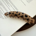 Dettaglio del fermaglio a banana leopardato con trama a guscio di tartaruga su un libro - Leopardo Beige