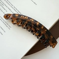 Dettaglio del fermaglio a banana leopardato con trama in resina ambrata su un libro - Leopardo Caffè