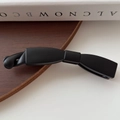 Fermaglio a banana nero opaco minimalista esposto su una superficie rustica in legno scuro - Satinato / Nero
