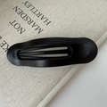 Barrette ovale noire mate minimaliste avec finition texturée sur fond de tissu beige - Noir Mat (environ 11,5 cm)