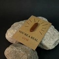 Detail van rood zandstenen kristalprisma op een YOU'RE A REAL GEM cadeaukaart met steen - Gouden zandsteen