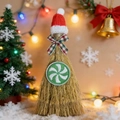 Kerstversiering bezem van stro met kerstmuts en rode strik in een sfeervolle kerstboom omgeving - Rode Muts Pepermuntje
