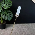 Detail view of white crystal column with gold metal wire stand on grey textured mat - White Crystal