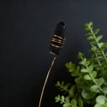 Close-up of natural black crystal pillar wrapped in golden copper wire on black background - Black