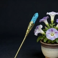 Close-up of a gold hair stick with intricate floral filigree and a blue stone inlay - Turquoise