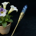 Close-up of handmade golden hair pin featuring a hexagonal blue crystal and hollow floral patterns - Blue Sodalite