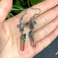 Detail of silver turtle earrings with wire-wrapped rainbow crystal prisms on palm - Green and Pink