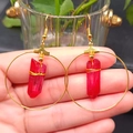 Detail of bohemian gold hoop earrings featuring red crystal pendants held by hand - Red & Gold Hoop