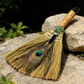 Close-up of decorative witch broom with peacock feather and dragon charm on rock - Obsidian Viking Dragon Broom