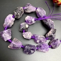 Detailed view of raw natural amethyst stones strung on purple cord over black background - Purple Crystal