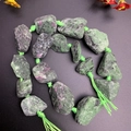 Macro shot of raw unpolished ruby zoisite stones with green woven cord and tassel - Unakite
