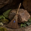 Detalle de mini escoba de bruja con pentagrama de bronce y cristal azul sobre rocas con musgo - Pentagrama Bronce Cristal Azul