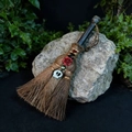 Detail of handcrafted witch broom with skull charm and rose on a natural rock background - White Skull Style (03)