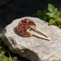 Close-up of golden crescent hair clip with natural reddish-brown stone inlay on grey rock - Red Jasper