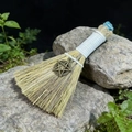 Detailed close-up of a mini handmade witch broom with a bronze pentagram charm on a mossy rock - Apatite And Pentagram