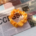 Vibrant yellow silk satin scrunchie with soft ruffles on vintage newspaper backdrop - Orange