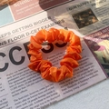 Vibrant orange satin scrunchie accessory displayed on a vintage newspaper background - Orange Red
