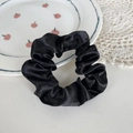 Elegant black satin scrunchie with high glossy texture on a white decorative background plate - Black