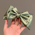 Grande pince à cheveux nœud en satin vert sauge avec texture soyeuse en main - Vert