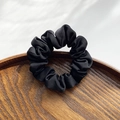 Elegante coletero de satén negro con textura plisada suave en una bandeja de madera - Negro