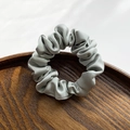 Elegant sage green satin hair scrunchie with silky texture on a wooden tray - Green
