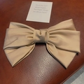 Champagne gold satin bow hair claw clip with elegant silk texture on leather background - Camel