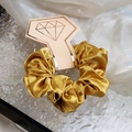 Glossy golden satin scrunchie presented on a pink geometric display card with gold logo - Yellow