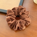 Brown velvet scrunchie hair tie with pleated texture on a warm wooden surface - Brown