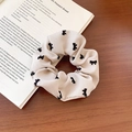 Beige floral scrunchie with black velvet bow print on rustic wooden desk background - Off White