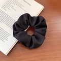 Elastic black scrunchie with embroidered bows on striped fabric in a lifestyle setting - Black